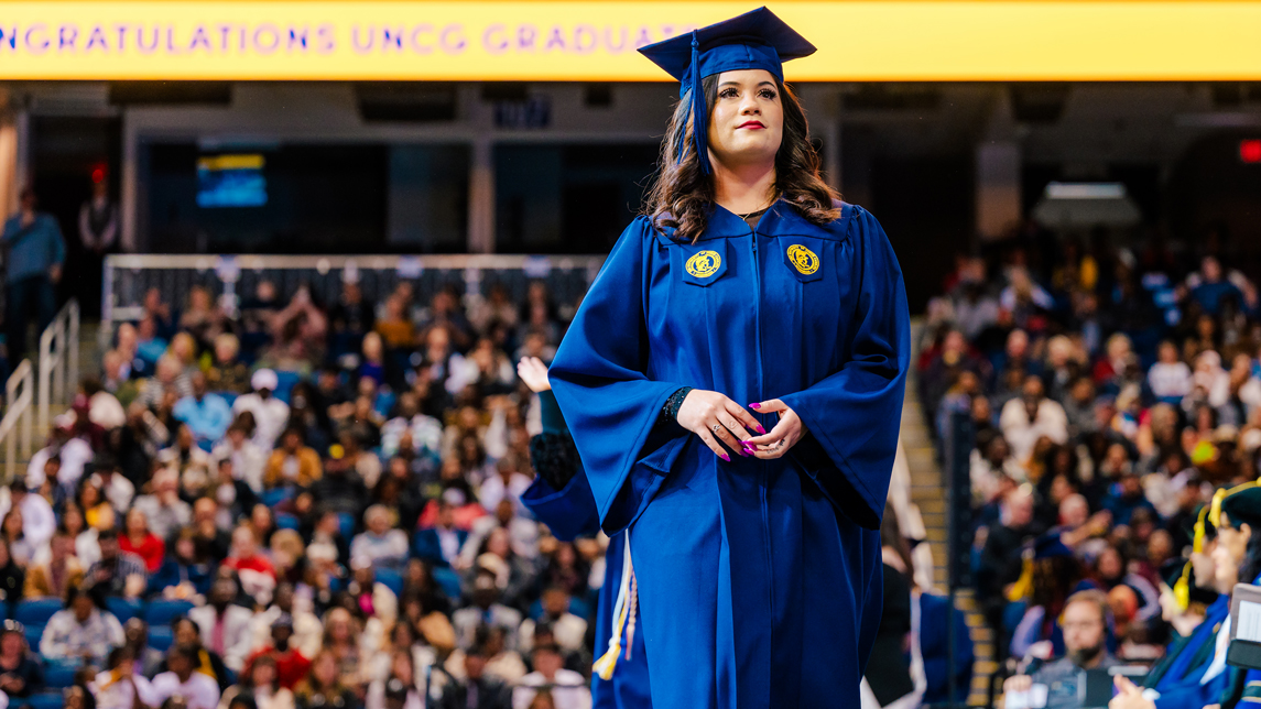 A graduate walks across stage at the December 2023 UNCG commencement.